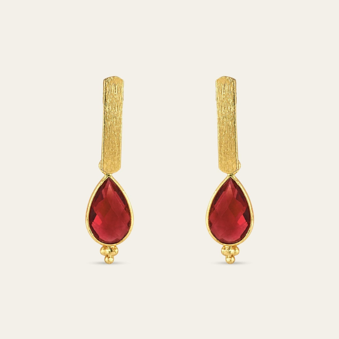Aros con soporte de palito satinado enchapado en oro de 18 kt con colgante gota facetada en color rojo, sobre fondo blanco - Coca Johnson Joyas - Chile
