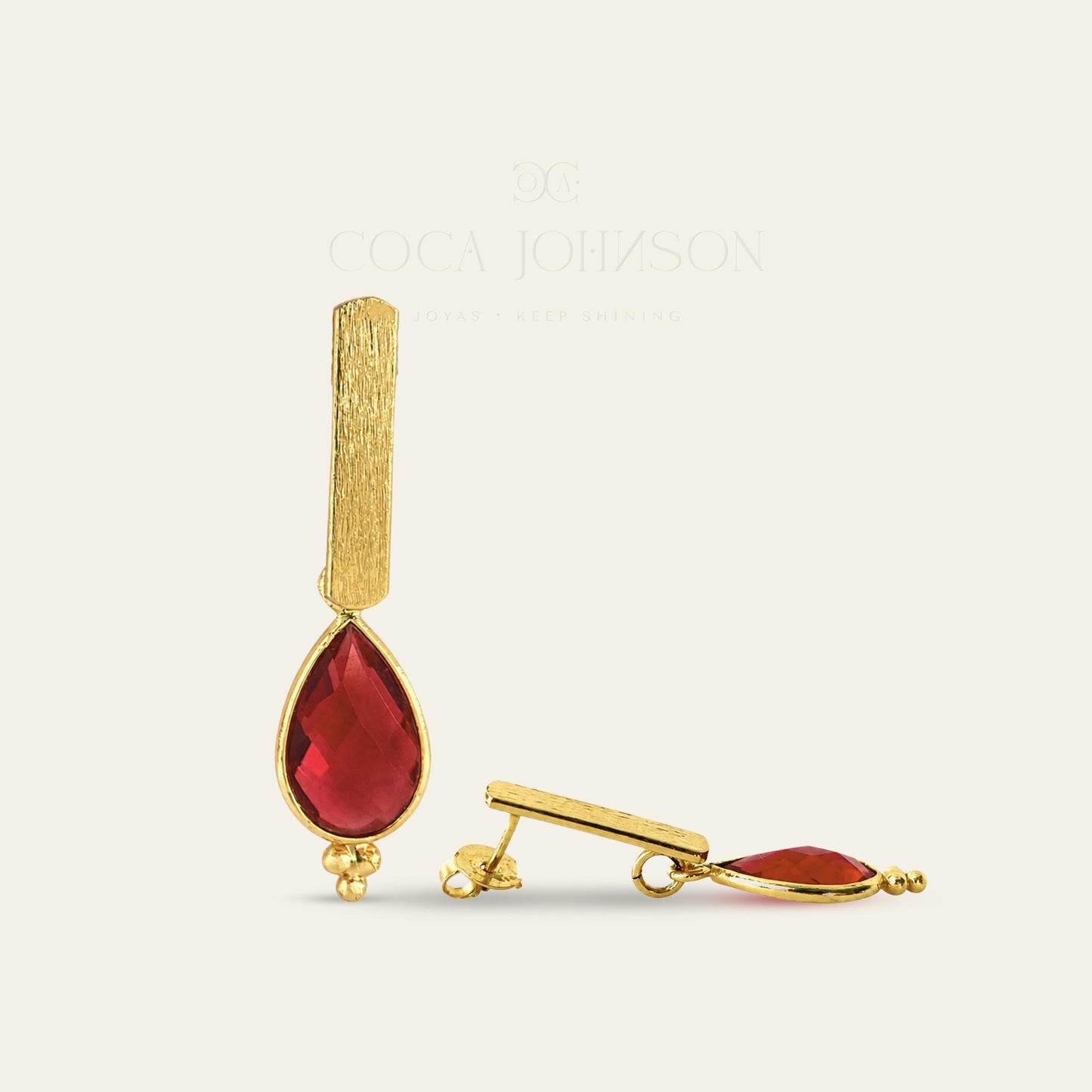 Aros con soporte de palito satinado enchapado en oro de 18 kt con colgante gota facetada en color rojo, de frente y lado sobre fondo blanco - Coca Johnson Joyas - Chile