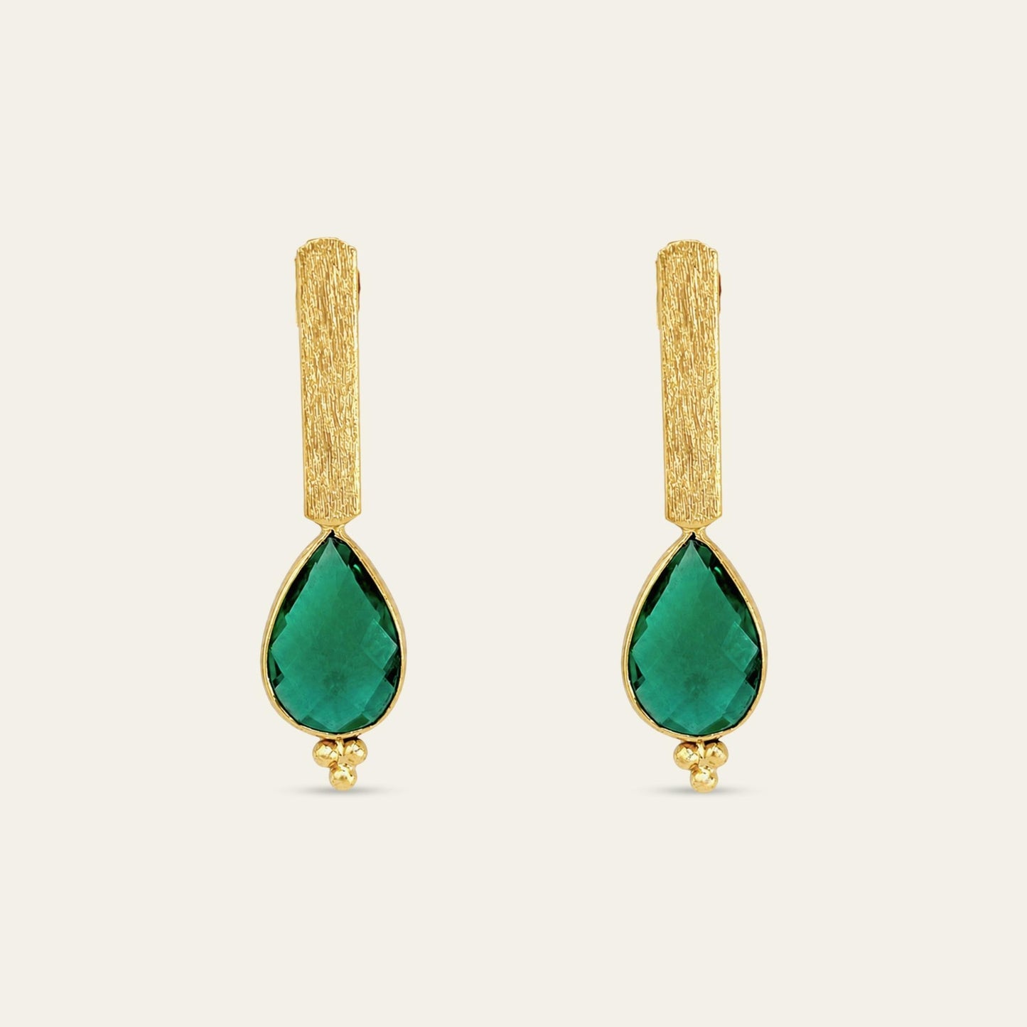 Aros con soporte de palito satinado enchapado en oro de 18 kt con colgante gota facetada en color verde esmeralda, sobre fondo blanco - Coca Johnson Joyas - Chile