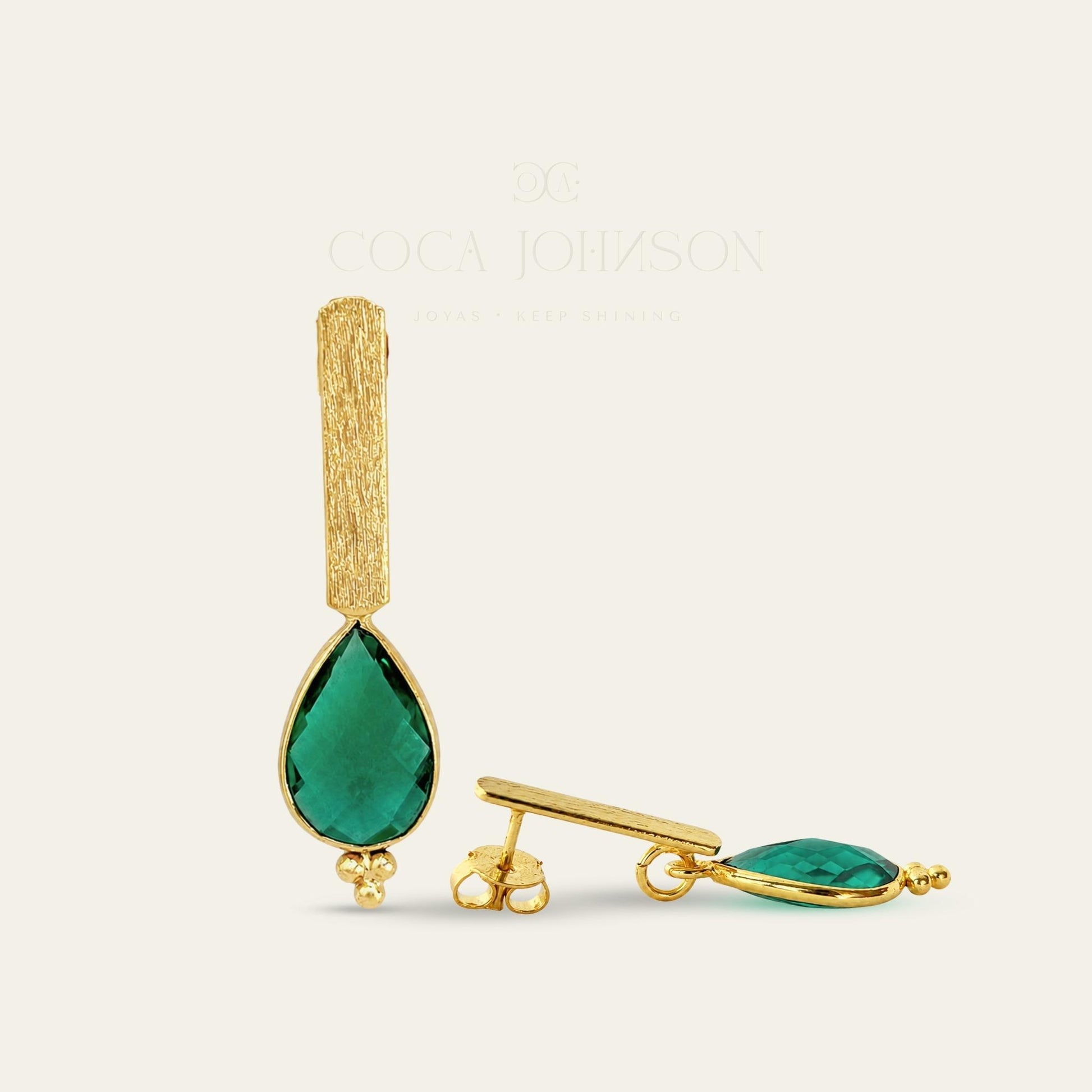 Aros con soporte de palito satinado enchapado en oro de 18 kt con colgante gota facetada en color verde esmeralda, de frente y lado sobre fondo blanco - Coca Johnson Joyas - Chile