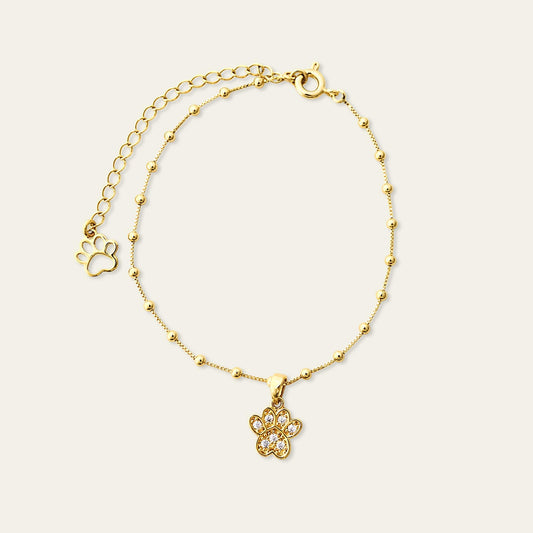 Pulsera con charm de patita de perro y circones,  enchapada en oro de 18kt, sobre fondo blanco - Coca Johnson Joyas - Chile