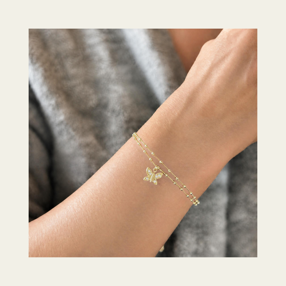 Zoom en muñeca de mujer usando pulsera doble con colgante de mariposa con circones